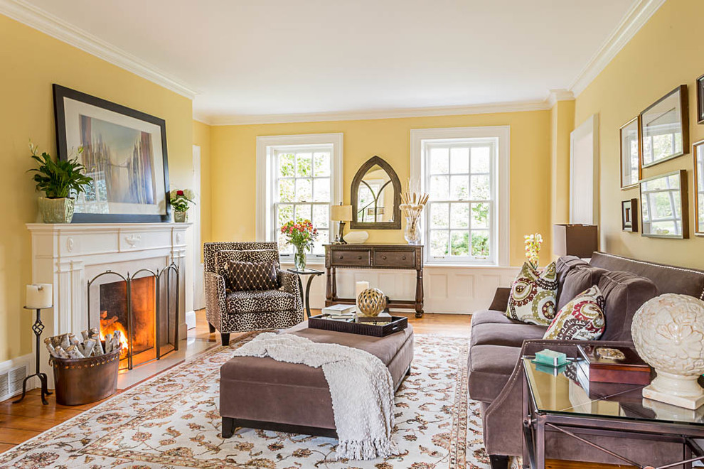 Réalisation d'une salle de séjour tradition de taille moyenne et fermée avec un mur jaune, un sol en bois brun, une cheminée standard et un manteau de cheminée en béton.