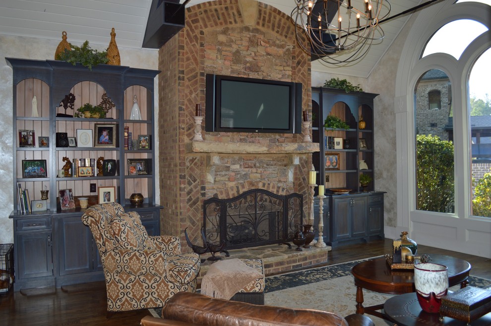Inspiration pour une grande salle de séjour traditionnelle ouverte avec un mur gris, un sol en bois brun, une cheminée standard, un manteau de cheminée en pierre et un téléviseur fixé au mur.
