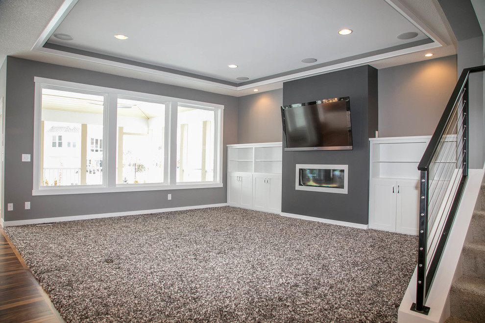Modelo de sala de estar abierta minimalista con paredes grises, moqueta, chimenea lineal, marco de chimenea de metal y televisor colgado en la pared