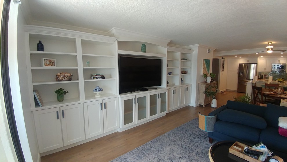 This is an example of a large beach style open plan games room in Tampa with white walls, light hardwood flooring, a built-in media unit and brown floors.