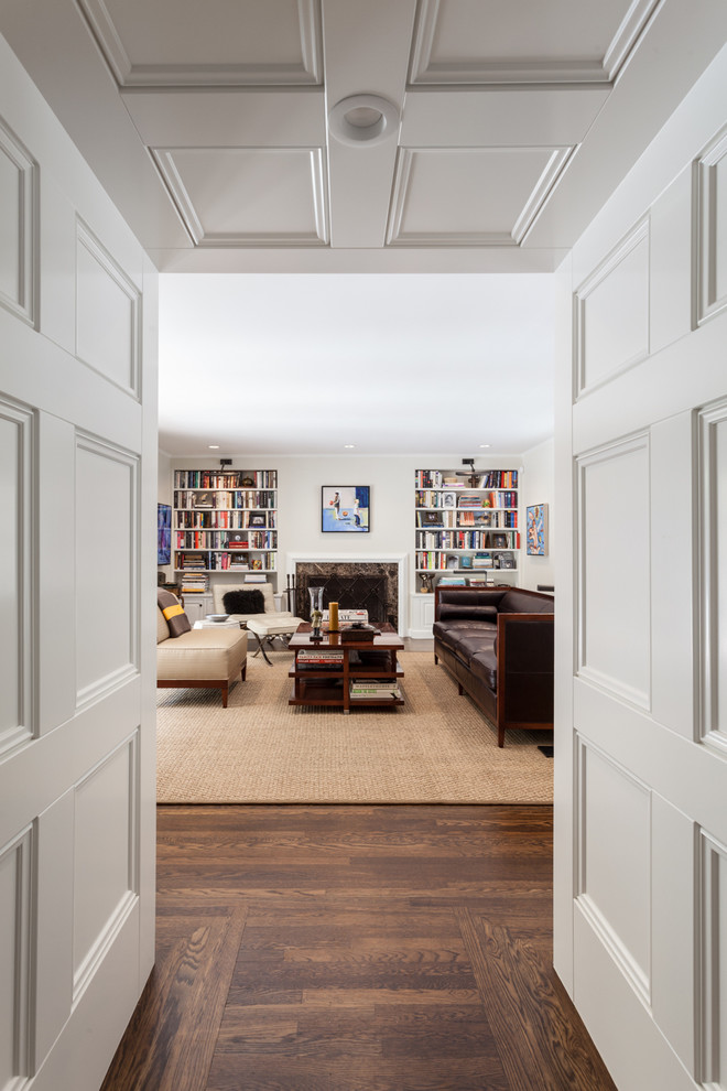 Imagen de sala de estar con biblioteca abierta tradicional grande con paredes blancas, suelo de madera oscura, todas las chimeneas, marco de chimenea de piedra y televisor colgado en la pared