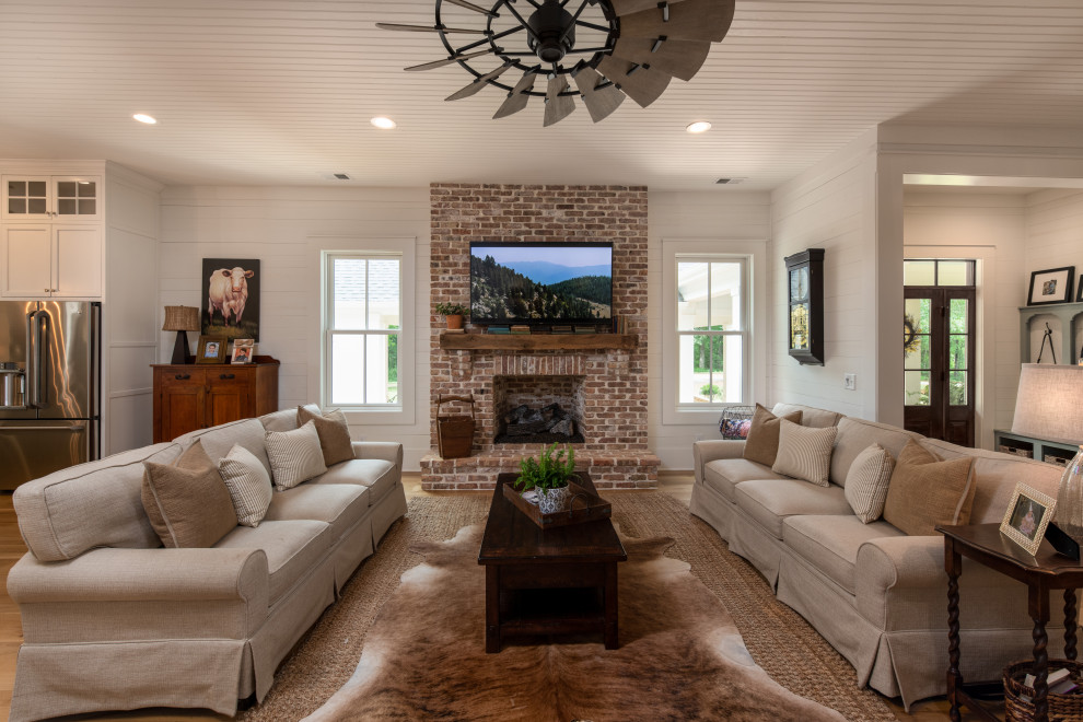 Inspiration for a large farmhouse open plan games room in Other with white walls, light hardwood flooring, a standard fireplace, a brick fireplace surround, a wall mounted tv and beige floors.