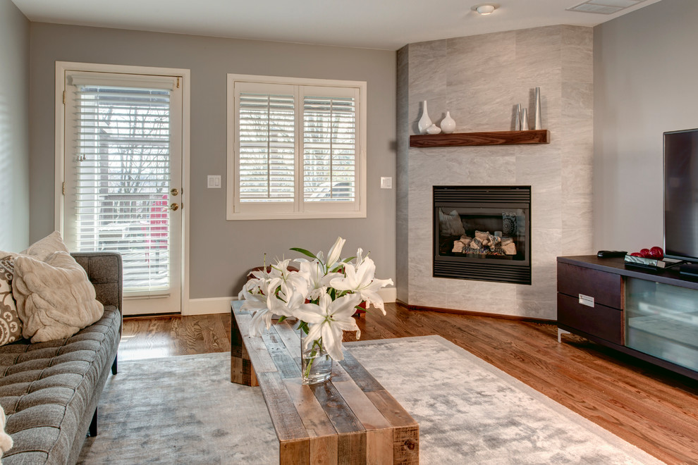 Exemple d'une salle de séjour tendance de taille moyenne et ouverte avec un mur gris, un sol en bois brun, une cheminée d'angle, un manteau de cheminée en carrelage et un téléviseur indépendant.