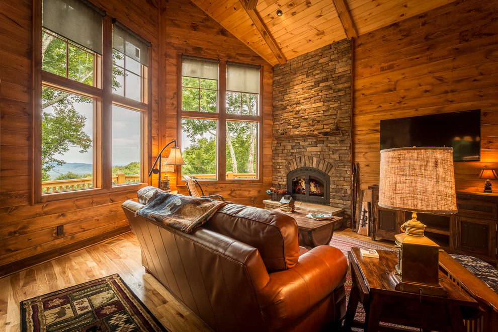Example of a mid-sized mountain style open concept medium tone wood floor and brown floor family room design in Charlotte with brown walls, a standard fireplace, a stone fireplace and a wall-mounted tv