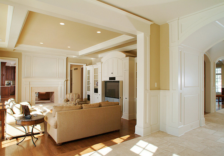 Diseño de sala de estar abierta clásica con paredes beige, suelo de madera en tonos medios, chimenea de doble cara, marco de chimenea de piedra y pared multimedia