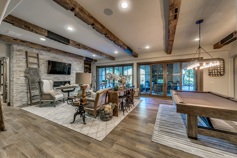 Inspiration for a large transitional open concept medium tone wood floor and brown floor game room remodel in Oklahoma City with white walls, a ribbon fireplace, a wall-mounted tv and a stone fireplace