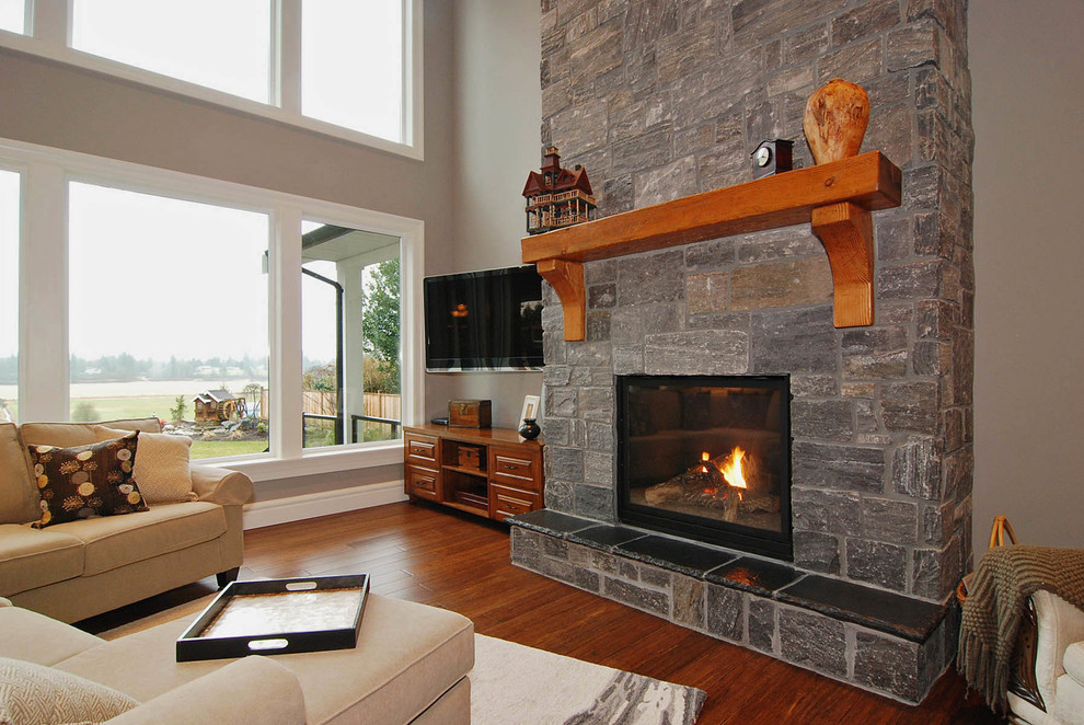Cette image montre une salle de séjour craftsman ouverte avec un mur gris, un sol en bois brun, un manteau de cheminée en pierre, salle de jeu, une cheminée standard et un téléviseur fixé au mur.
