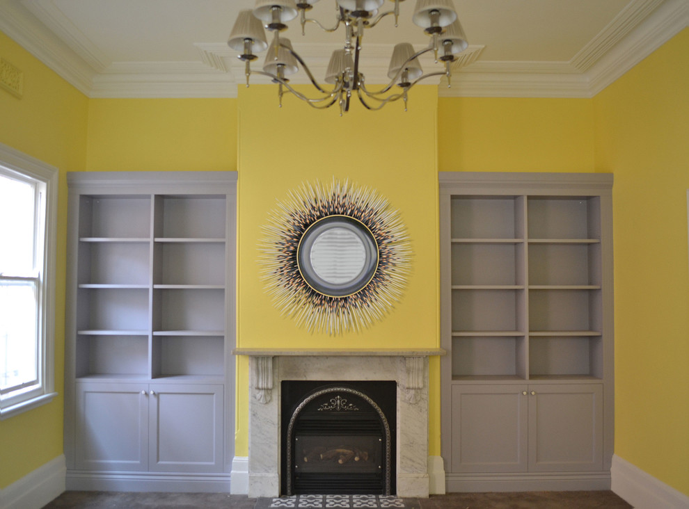 Immagine di un soggiorno minimal di medie dimensioni con libreria, pareti gialle, moquette, camino classico, cornice del camino in pietra e pavimento marrone