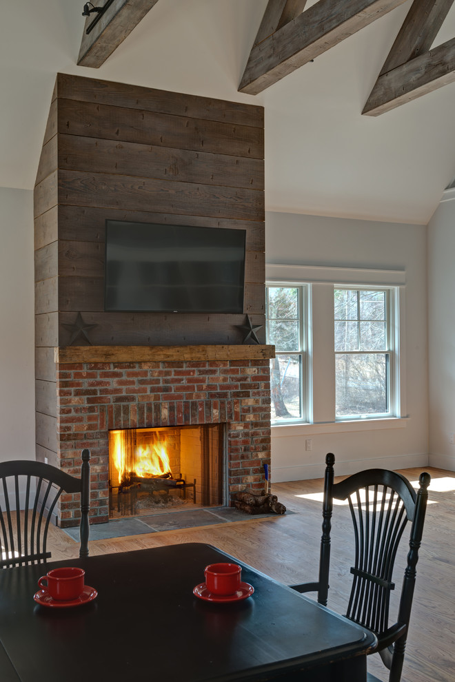 Photo of a large classic open plan games room in New York with white walls, a standard fireplace, a brick fireplace surround, a wall mounted tv, medium hardwood flooring and brown floors.