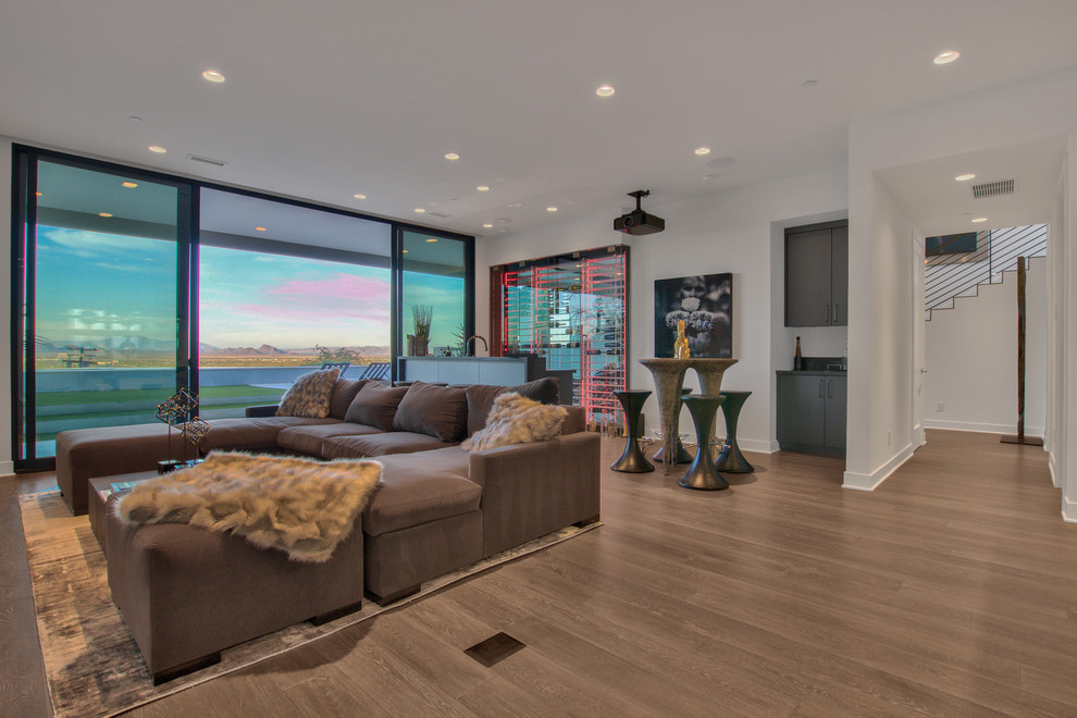 Cette image montre une grande salle de séjour design fermée avec un bar de salon, un mur blanc, un sol en bois brun, aucune cheminée, un téléviseur encastré et un sol marron.