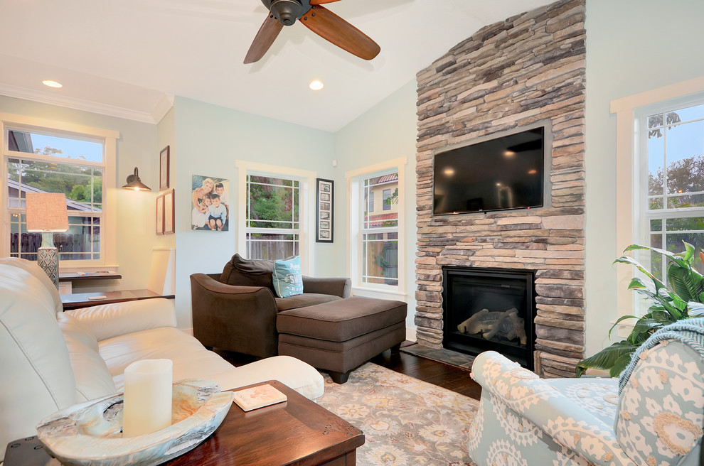 Imagen de sala de estar abierta de estilo americano de tamaño medio con paredes azules, suelo de madera en tonos medios, todas las chimeneas, marco de chimenea de piedra, televisor colgado en la pared y suelo marrón