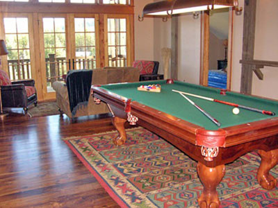 Photo of a large rustic open plan games room in Other with a game room, beige walls, dark hardwood flooring, a standard fireplace, a stone fireplace surround and a concealed tv.