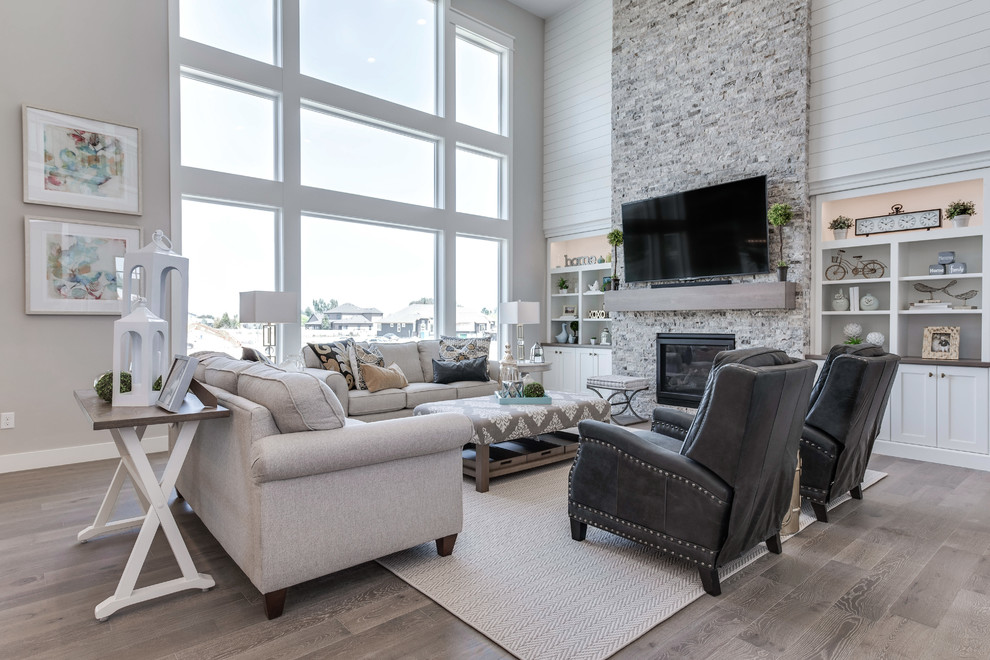 Modelo de sala de estar abierta tradicional grande con paredes grises, suelo laminado, todas las chimeneas, marco de chimenea de ladrillo, televisor colgado en la pared y suelo gris