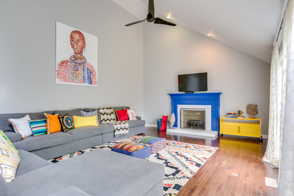 Modelo de sala de estar abierta contemporánea grande con paredes grises, suelo de madera en tonos medios, marco de chimenea de madera y televisor colgado en la pared