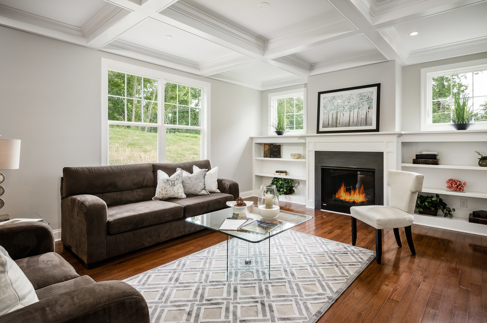 Ejemplo de sala de estar de estilo americano con paredes grises, suelo de madera en tonos medios y marco de chimenea de madera