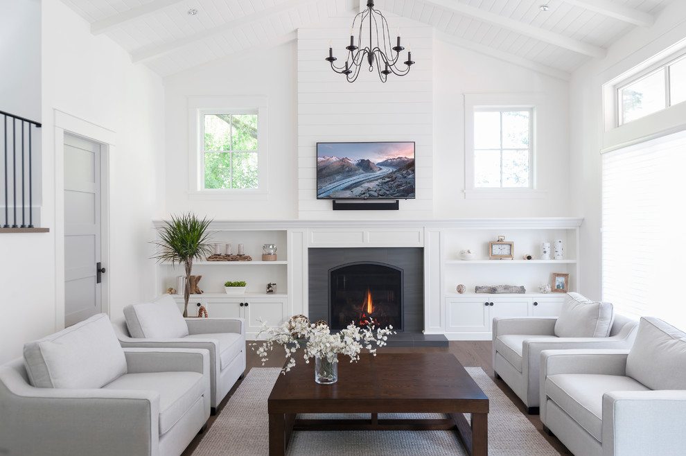 На фото: гостиная комната в морском стиле с белыми стенами, темным паркетным полом, стандартным камином, телевизором на стене, коричневым полом и ковром на полу