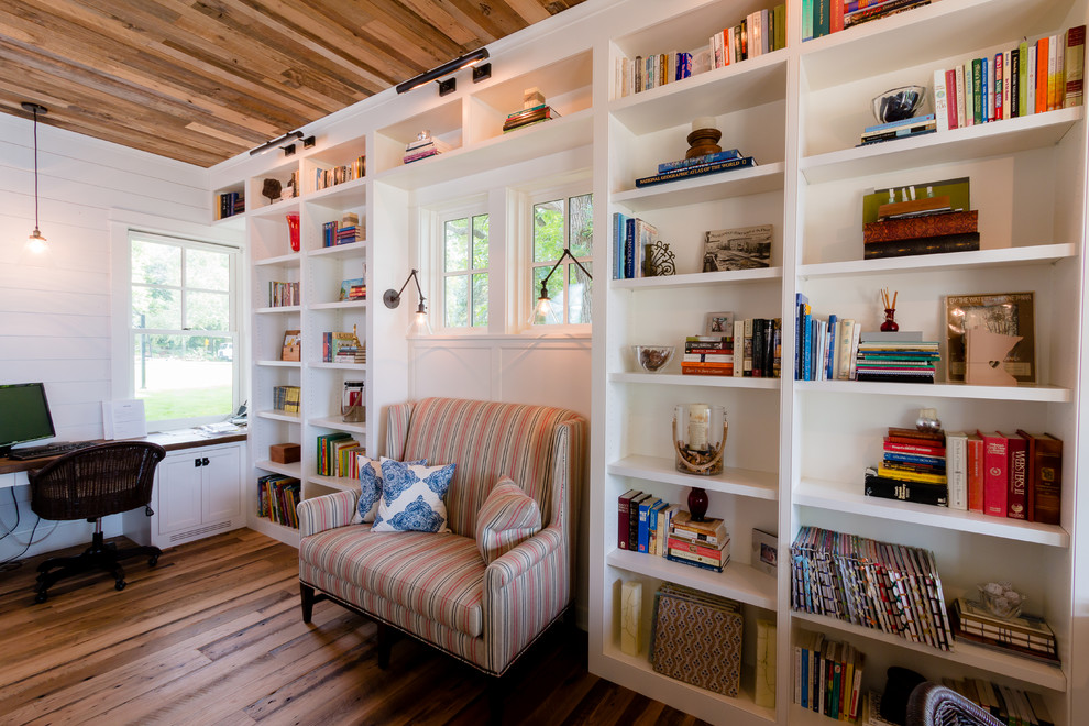 Foto på ett mellanstort lantligt avskilt allrum, med ett bibliotek, vita väggar, mellanmörkt trägolv och en dubbelsidig öppen spis