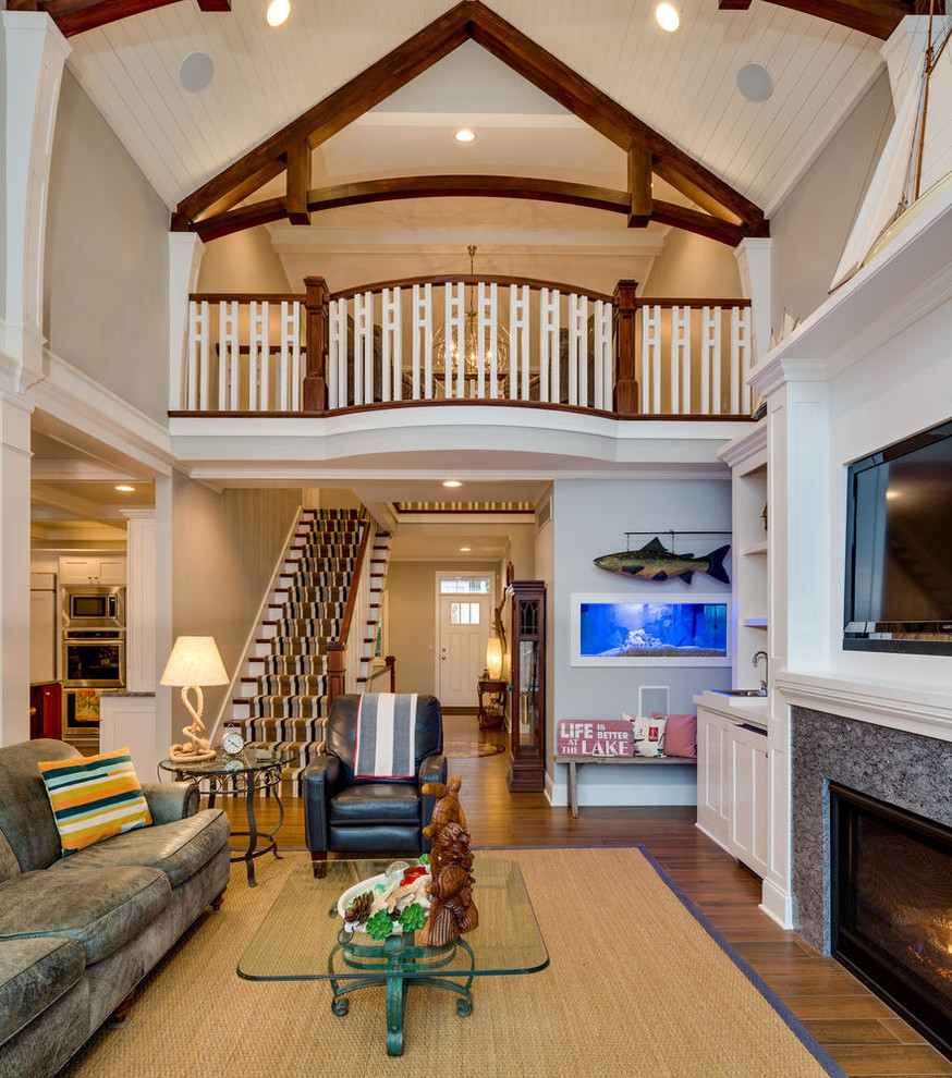 На фото: гостиная комната в морском стиле с серыми стенами, паркетным полом среднего тона, стандартным камином, телевизором на стене, коричневым полом и ковром на полу