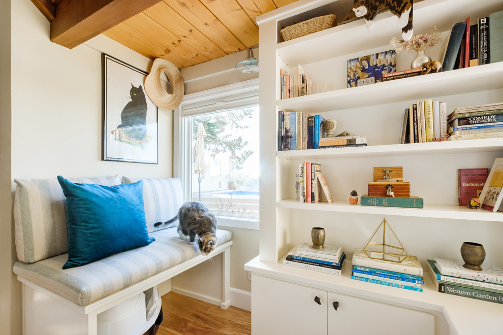 Diseño de sala de estar con biblioteca cerrada costera de tamaño medio sin chimenea con paredes beige, suelo de madera clara y suelo marrón
