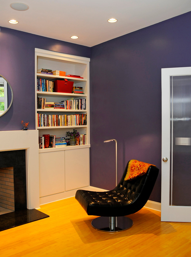 Esempio di un soggiorno minimalista con libreria, pareti viola, parquet chiaro, camino classico e cornice del camino in pietra