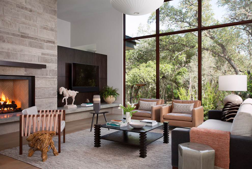 Example of a trendy light wood floor family room design in Austin with white walls, a standard fireplace, a stone fireplace and a wall-mounted tv