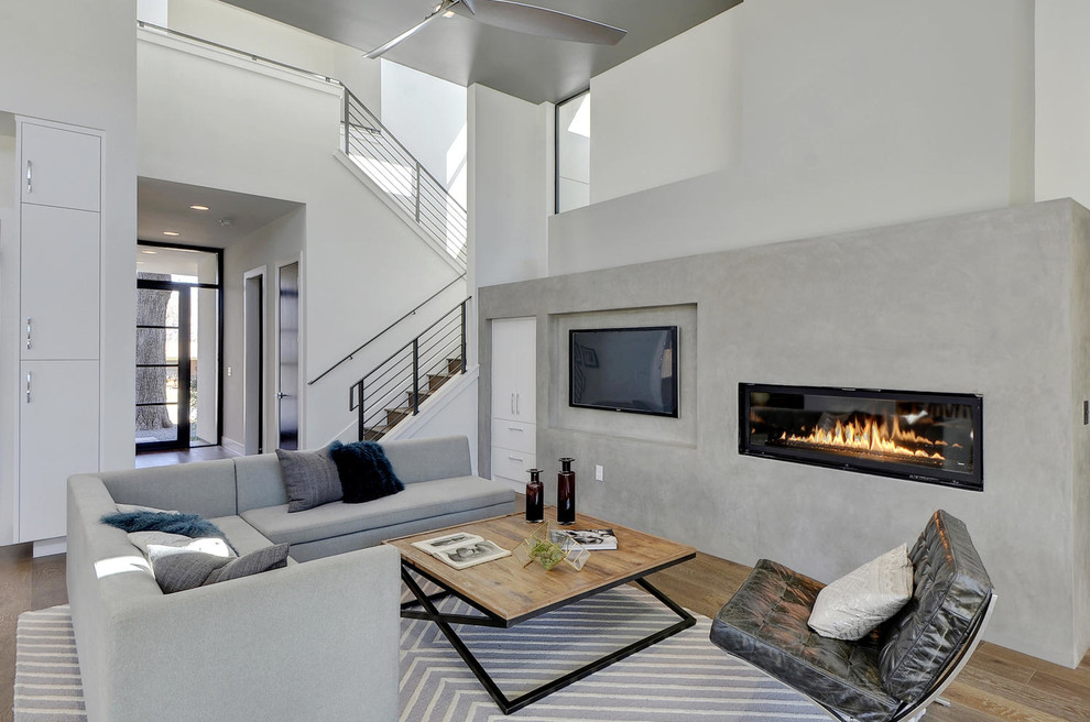 Diseño de sala de estar abierta actual con suelo de madera clara, chimenea lineal y televisor colgado en la pared
