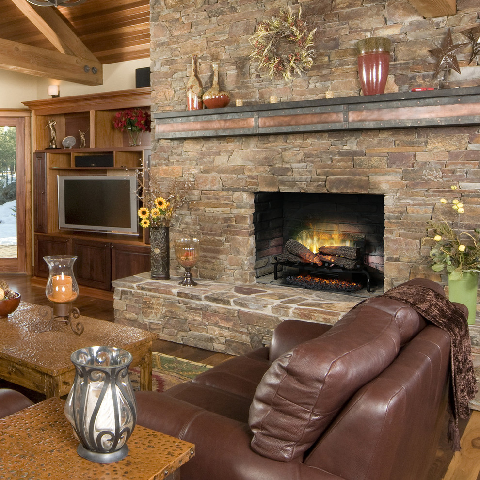 Inspiration for a medium sized rustic games room in Denver with medium hardwood flooring, a standard fireplace, a stone fireplace surround, a freestanding tv and brown floors.
