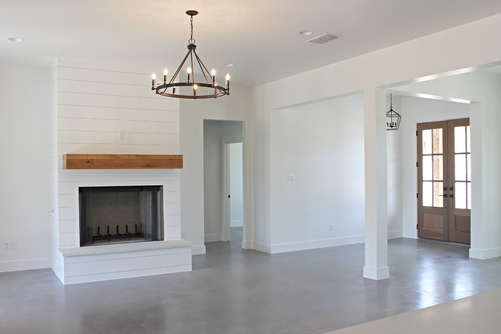Cette image montre une salle de séjour rustique avec un mur blanc, sol en béton ciré, une cheminée standard, un manteau de cheminée en bois et un sol gris.