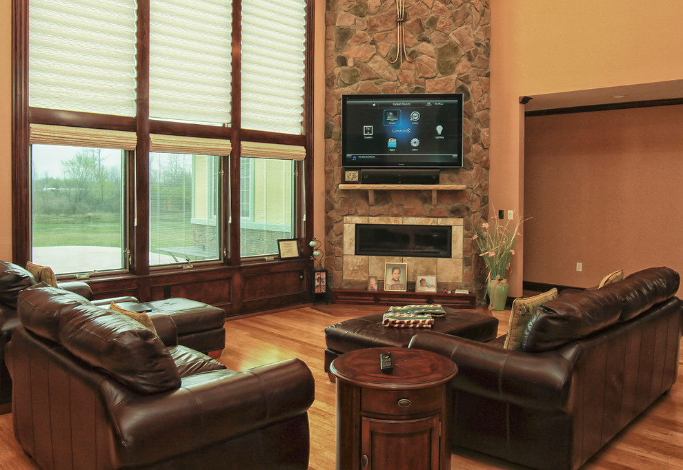 Ejemplo de sala de estar cerrada contemporánea grande con paredes beige, suelo de madera clara, chimenea de esquina, marco de chimenea de piedra y televisor colgado en la pared