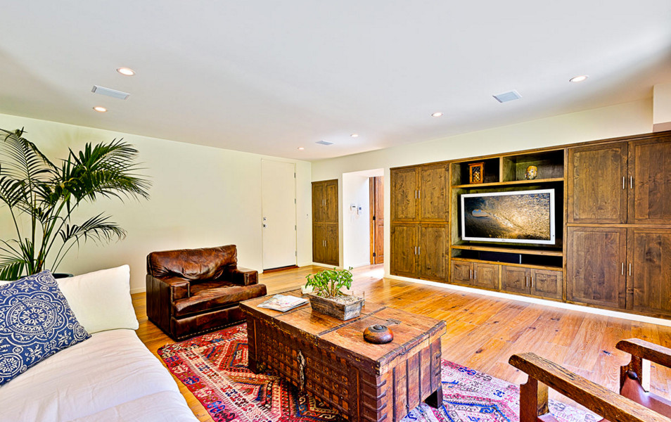 Imagen de sala de estar cerrada tropical de tamaño medio sin chimenea con paredes beige, suelo de madera clara, pared multimedia y suelo beige