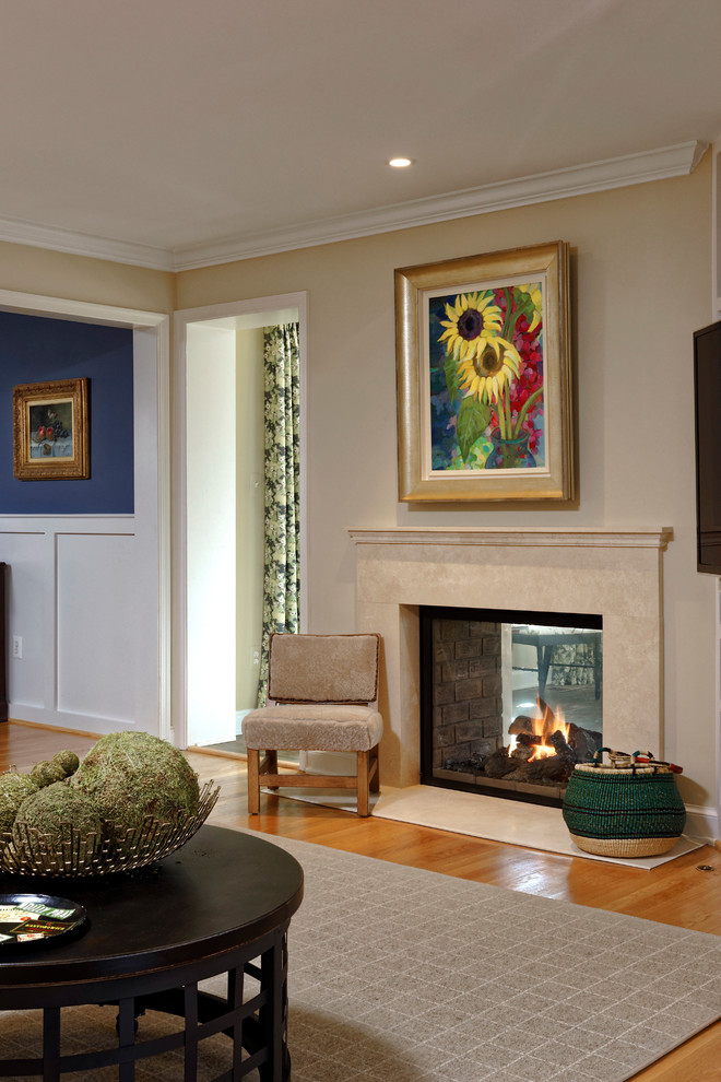 На фото: открытая гостиная комната в классическом стиле с паркетным полом среднего тона, двусторонним камином, фасадом камина из камня и телевизором в углу