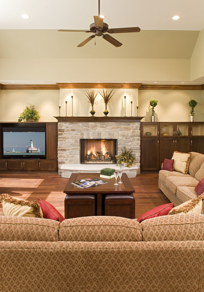Idées déco pour une grande salle de séjour craftsman ouverte avec un mur beige, un sol en bois brun, une cheminée standard, un manteau de cheminée en pierre et un téléviseur encastré.