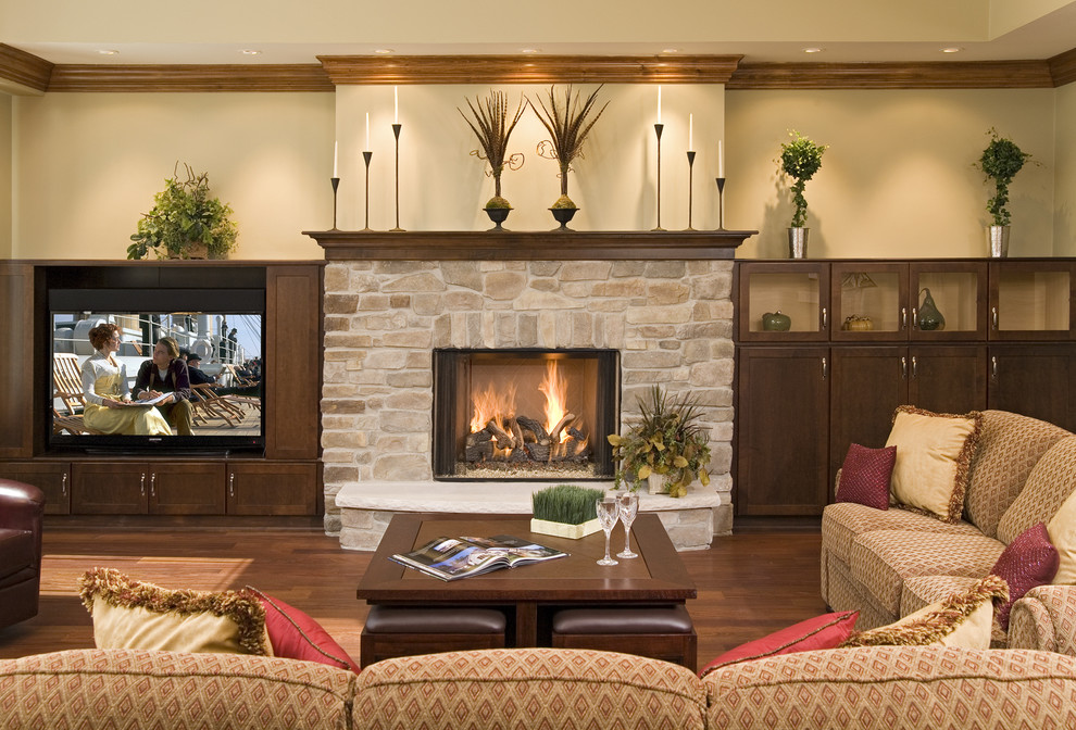 Ejemplo de sala de estar abierta de estilo americano grande con paredes beige, suelo de madera en tonos medios, todas las chimeneas, marco de chimenea de piedra y pared multimedia