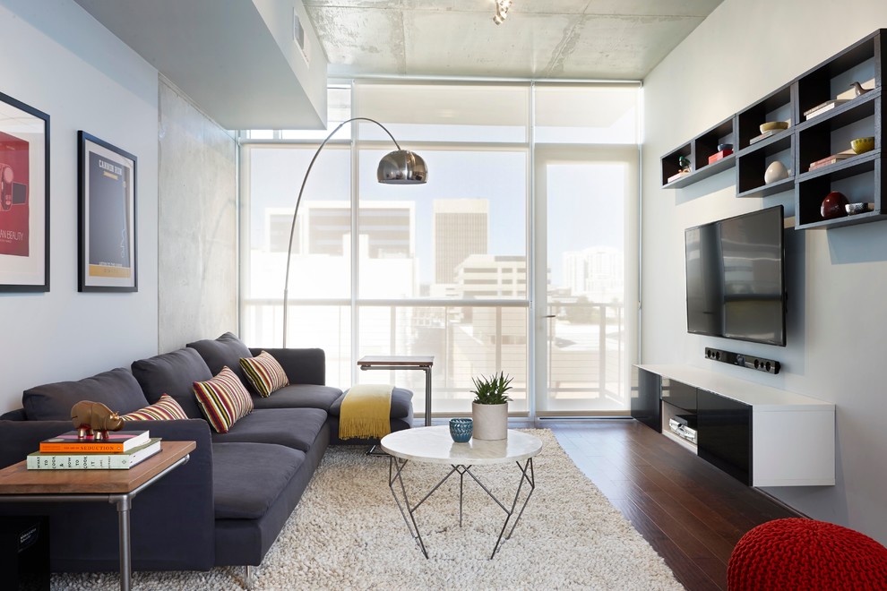 Стильный дизайн: открытая гостиная комната в современном стиле с белыми стенами, темным паркетным полом и телевизором на стене - последний тренд