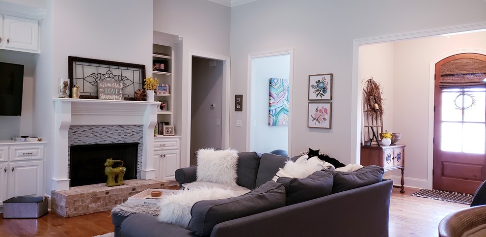 Diseño de sala de estar romántica grande con paredes grises, suelo de madera clara, todas las chimeneas, televisor colgado en la pared y suelo marrón