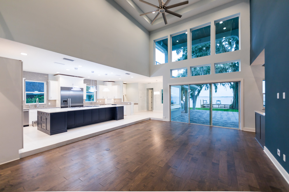 Example of a large tuscan open concept medium tone wood floor and brown floor family room design in Jacksonville with blue walls, a bar, a hanging fireplace and a wall-mounted tv