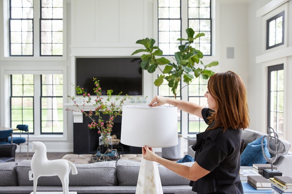 На фото: большая открытая гостиная комната в стиле неоклассика (современная классика) с белыми стенами, паркетным полом среднего тона, стандартным камином, фасадом камина из дерева, телевизором на стене и коричневым полом