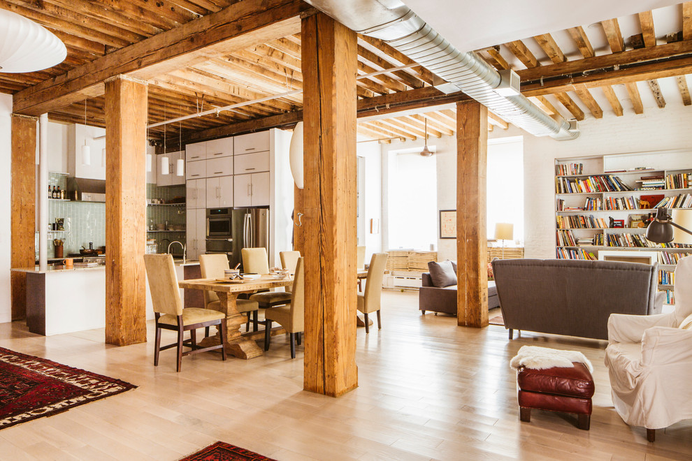 Imagen de sala de estar con biblioteca tipo loft urbana de tamaño medio sin televisor con paredes blancas, suelo de madera clara, todas las chimeneas y marco de chimenea de madera