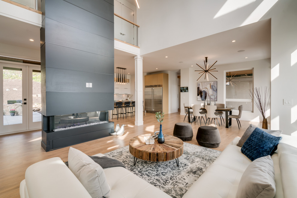 Inspiration for a large contemporary open plan games room in Vancouver with white walls, laminate floors, a two-sided fireplace, a timber clad chimney breast, a wall mounted tv and brown floors.