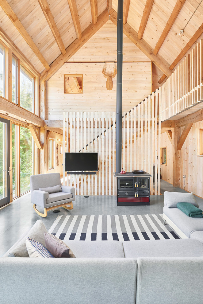 Ejemplo de sala de estar abierta rural con estufa de leña, marco de chimenea de metal, televisor colgado en la pared, suelo gris y alfombra