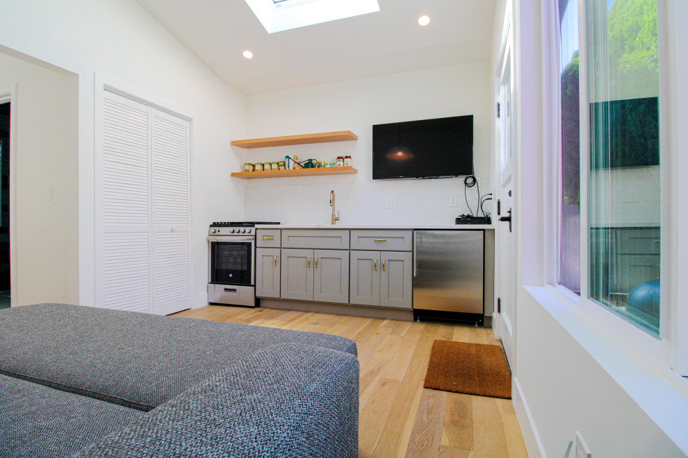 На фото: изолированная гостиная комната среднего размера в современном стиле с белыми стенами, телевизором на стене, полом из ламината, коричневым полом и сводчатым потолком с