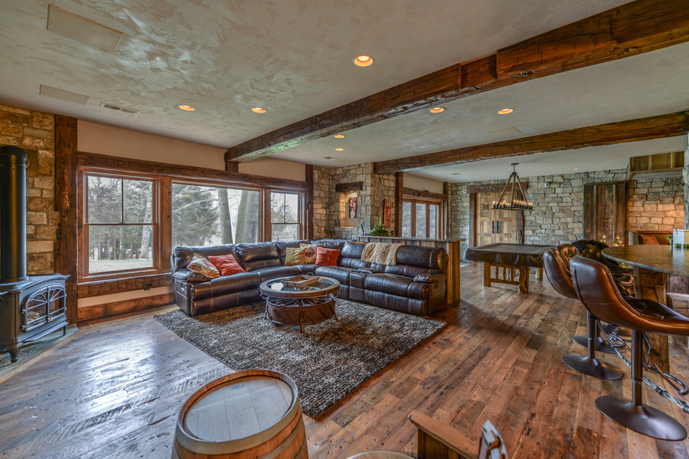 Inspiration for a large rustic open plan games room in Minneapolis with a game room, beige walls, medium hardwood flooring, a stone fireplace surround, a wall mounted tv and a wood burning stove.