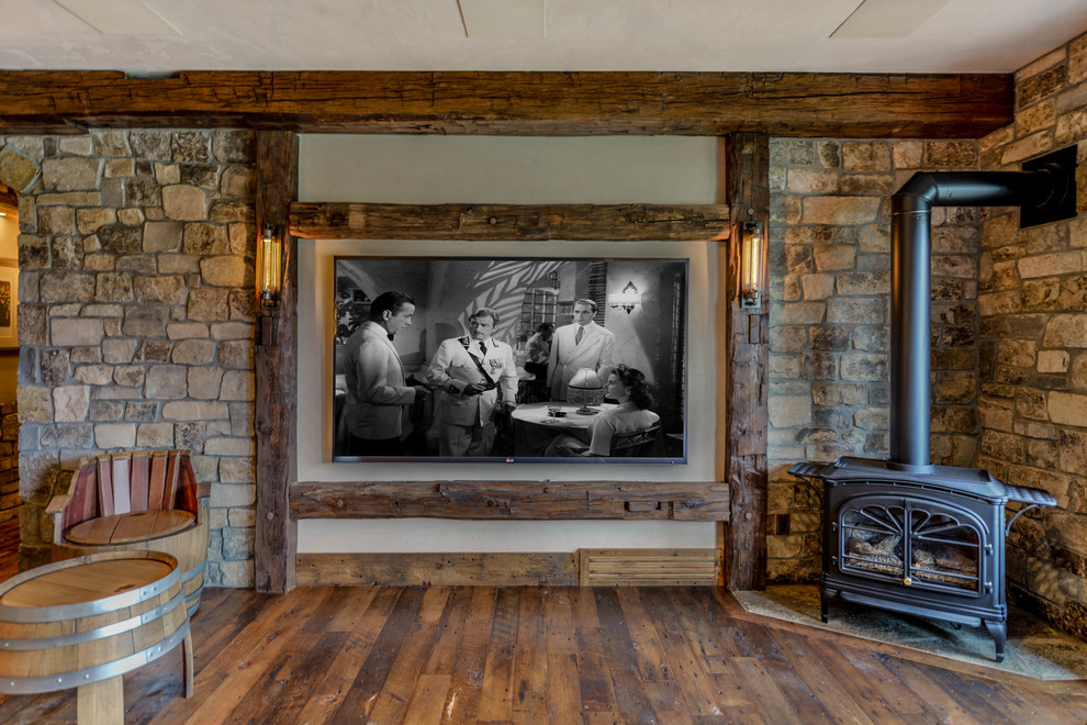 Imagen de sala de estar abierta rústica de tamaño medio con paredes beige, suelo de madera en tonos medios, marco de chimenea de piedra, televisor colgado en la pared y estufa de leña