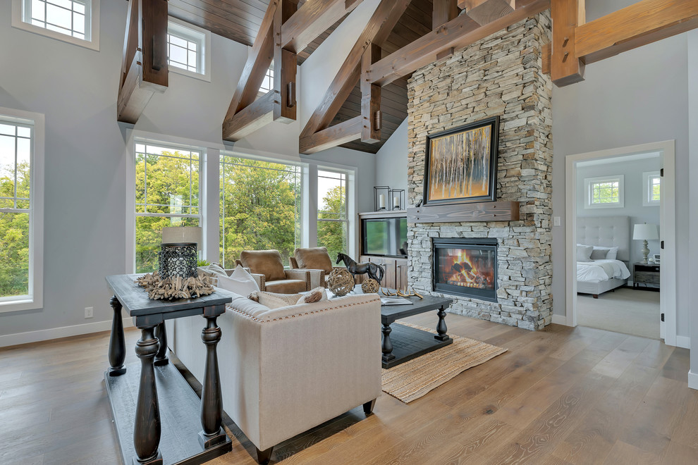 Example of a mid-sized arts and crafts open concept medium tone wood floor and brown floor family room design in Minneapolis with gray walls, a standard fireplace, a stone fireplace and a corner tv