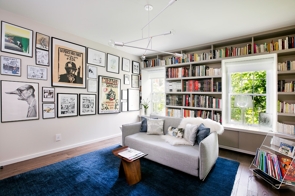 Cette photo montre une salle de séjour tendance avec une bibliothèque ou un coin lecture, un mur gris et un sol en bois brun.