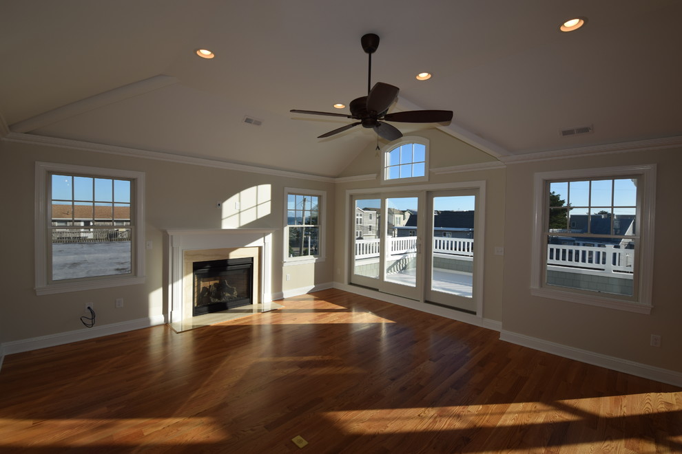 This is an example of a coastal open plan games room in New York with a home bar, white walls, medium hardwood flooring, a standard fireplace and a stone fireplace surround.