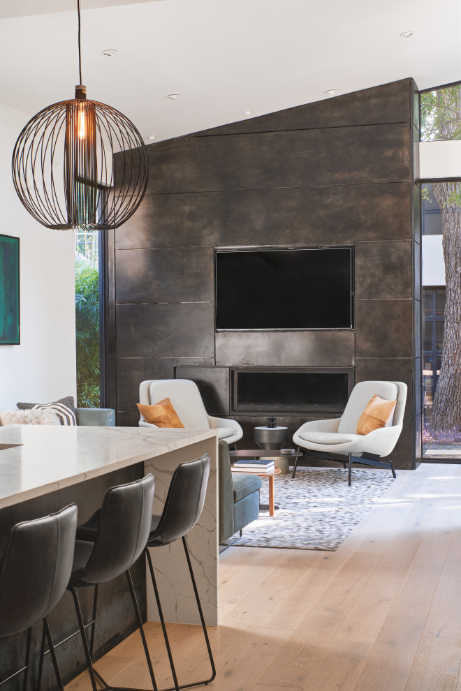 Aménagement d'une salle de séjour moderne ouverte avec un mur gris, parquet clair, cheminée suspendue, un manteau de cheminée en métal et un téléviseur fixé au mur.