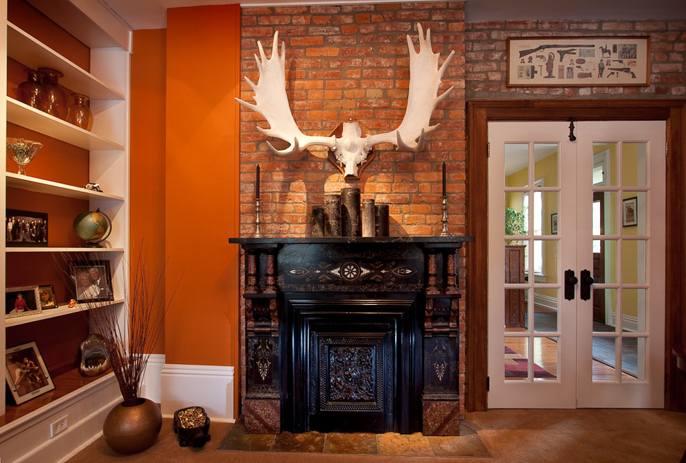 На фото: гостиная комната в стиле фьюжн с оранжевыми стенами и фасадом камина из дерева без телевизора с
