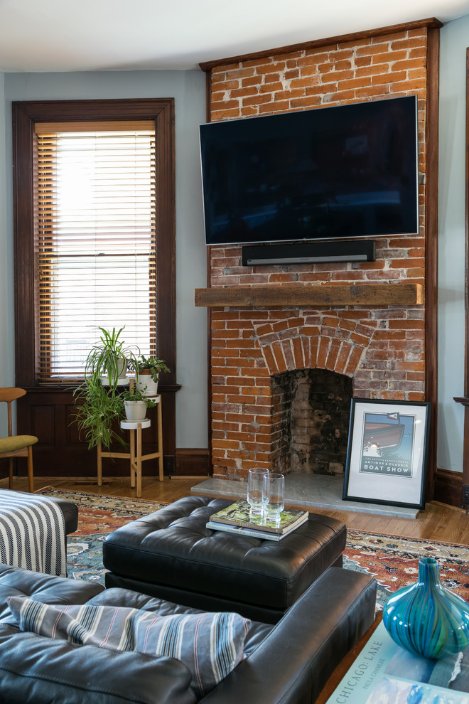 セントルイスにある中くらいなエクレクティックスタイルのおしゃれなファミリールーム (グレーの壁、無垢フローリング、標準型暖炉、レンガの暖炉まわり、壁掛け型テレビ) の写真