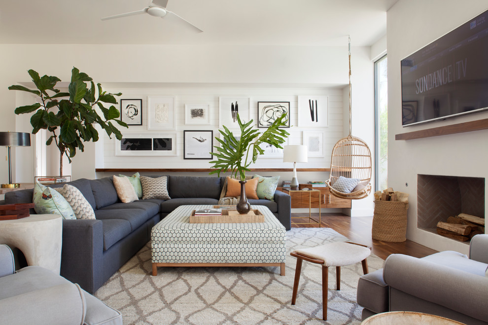 Large beach style open concept medium tone wood floor family room photo in Los Angeles with white walls, a standard fireplace, a plaster fireplace and a wall-mounted tv